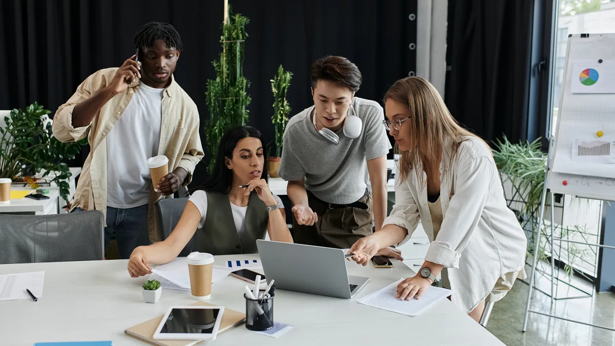 Équipe de quatre collègues réunis autour d'un ordinateur portable au bureau