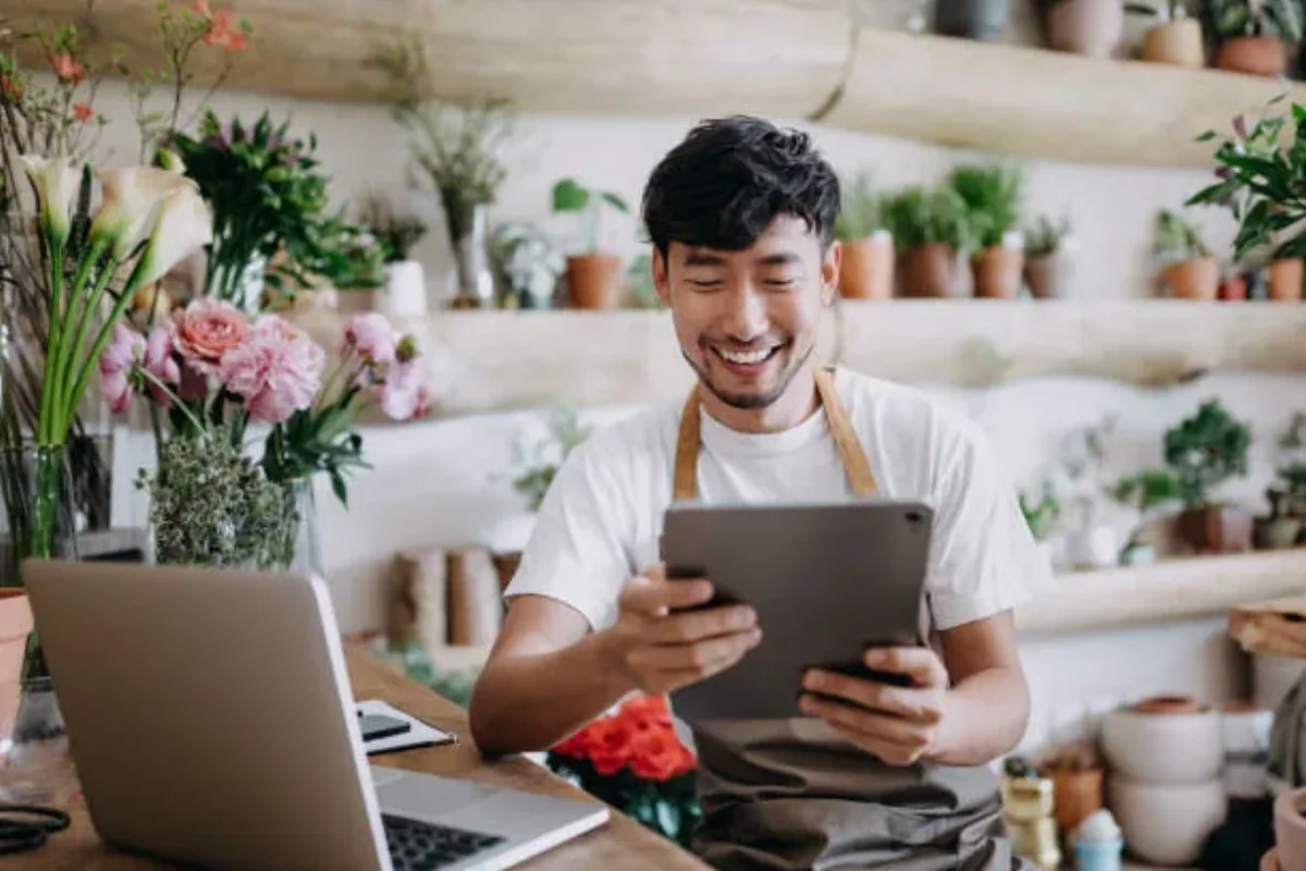 Fleuriste dans sa boutique consultant une tablette avant de préparer une campagne SMS clients