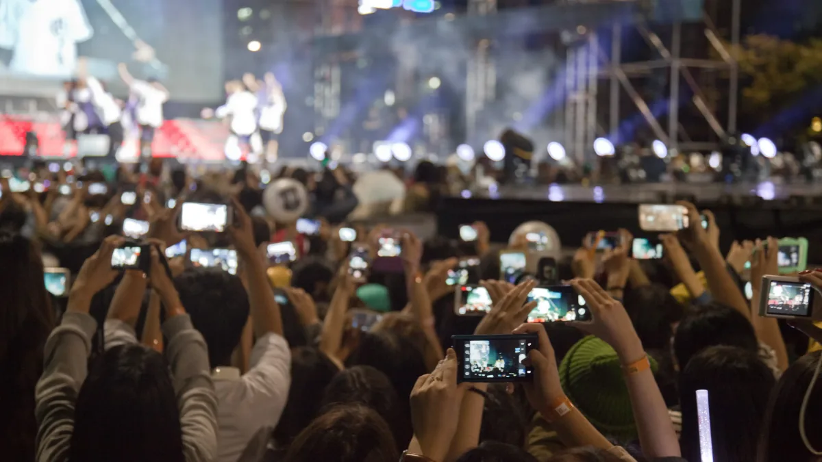 Public d'un concert en plein air filmant la scène avec des téléphones levés