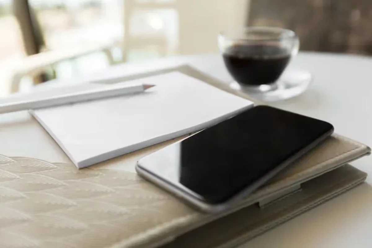 Smartphone posé sur un carnet à côté d'une tasse de café