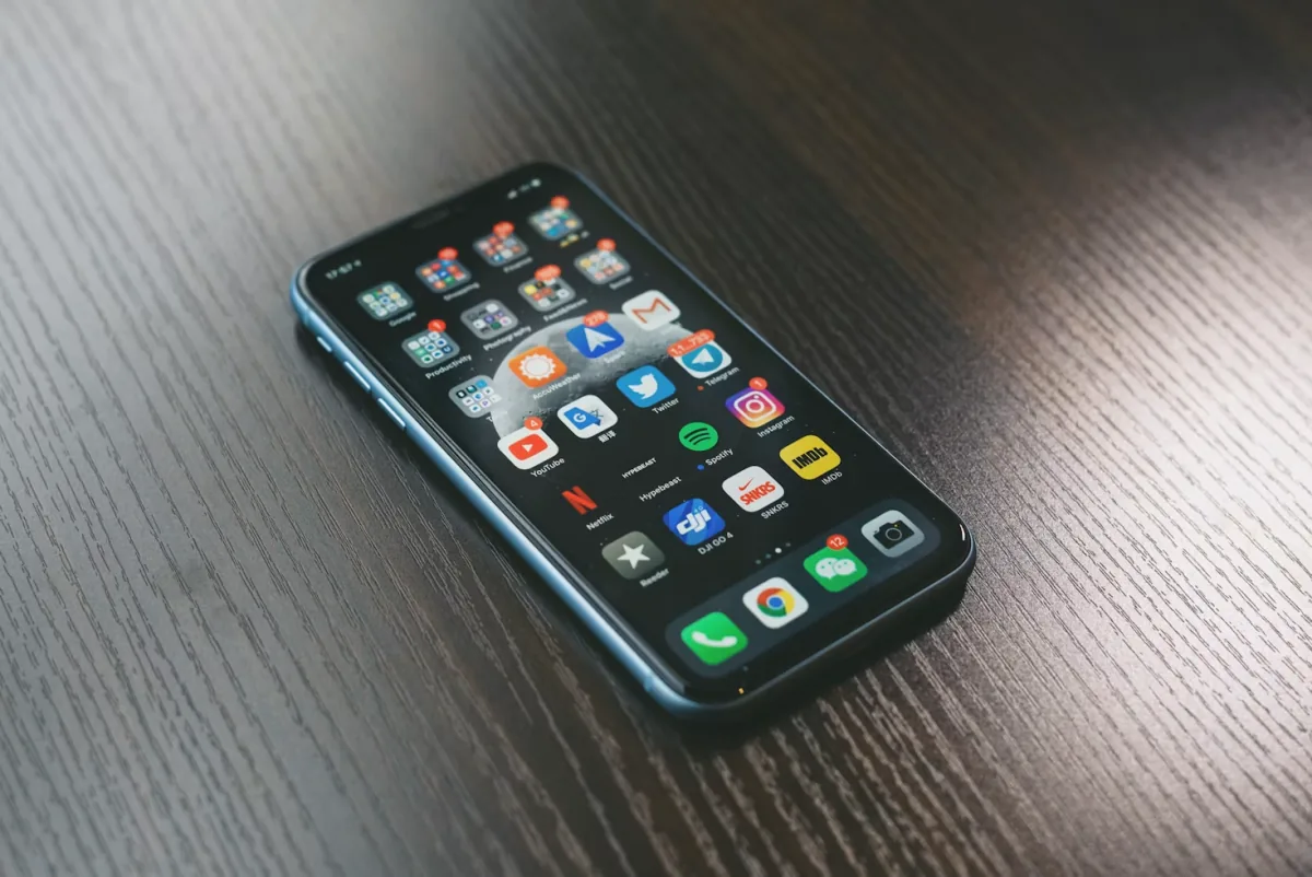Smartphone allumé affichant ses applications, posé sur un bureau en bois